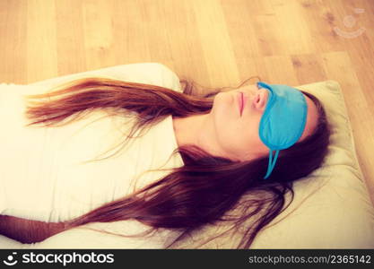 Sleep equipment concept. Portrait of brunette woman sleeping on floor in blue eye mask. Studio shot on beige background. Brunette woman sleeping in blue eye sleep mask