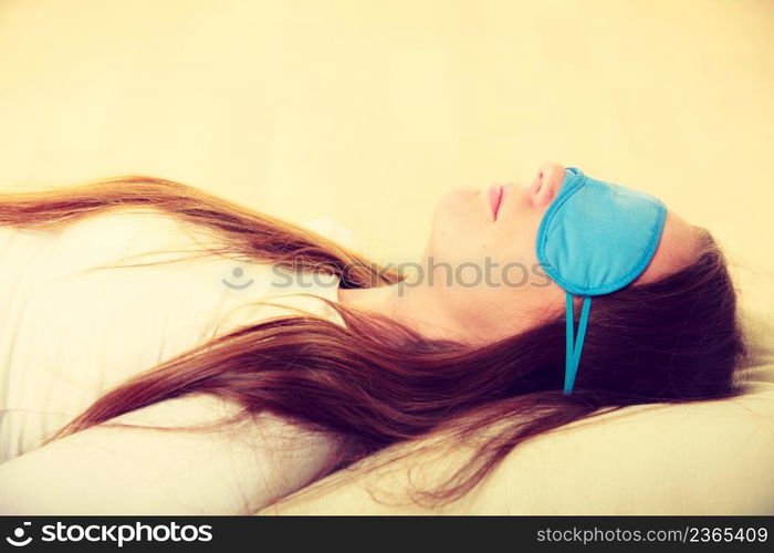 Sleep equipment concept. Portrait of brunette woman sleeping on floor in blue eye mask. Studio shot on beige background. Brunette woman sleeping in blue eye sleep mask