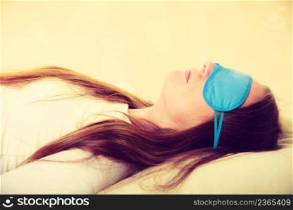 Sleep equipment concept. Portrait of brunette woman sleeping on floor in blue eye mask. Studio shot on beige background. Brunette woman sleeping in blue eye sleep mask