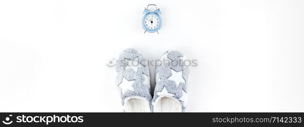 Sleep. Soft fluffy slippers and blue alarm clock isolated on white background. Creative conceptual top view flat lay in minimal style. Rest, good night, insomnia, relaxation, tired, hygge concept