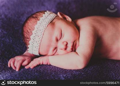 Sleeping baby with a white lace on his head lying on stomach on purple blanket. Portrait of charming sleeping baby