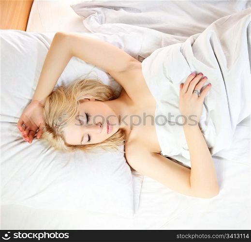 Sleeping blonde at white cotton bedclothes.