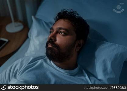 sleeping, insomnia and people concept - speelpess indian man lying in bed at home at night. speelpess indian man lying in bed at night