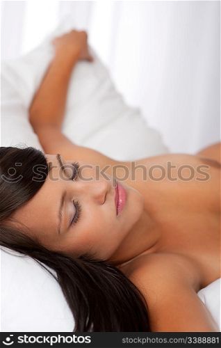 Sleeping naked brown hair woman in white bed, shallow DOF