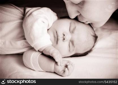 Sleeping newborn baby closeup face with mother kissing