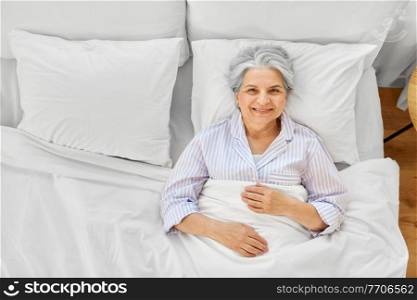 sleeping, old age and people concept - happy smiling awake senior woman lying in bed at home bedroom. smiling senior woman lying in bed at home bedroom