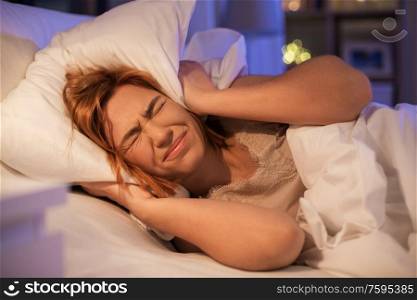 sleeping problem, insomnia and people concept - annoyed woman covering ears with pillow in bed at night. annoyed woman suffering from insomnia at night