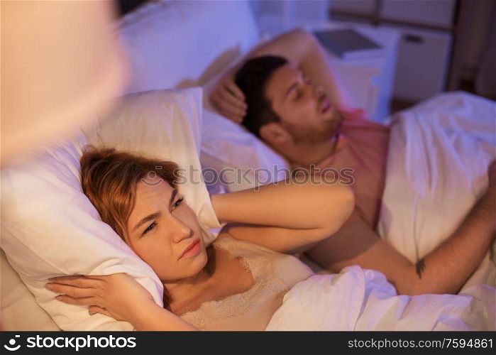 sleeping problem, insomnia and people concept - woman suffering from snoring man and covering ears with pillow in bed at home. woman suffering from insomnia or snoring man
