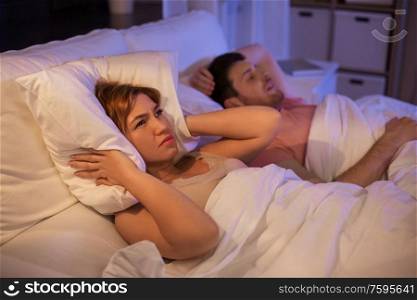 sleeping problem, insomnia and people concept - woman suffering from snoring man and covering ears with pillow in bed at home. woman suffering from insomnia or snoring man