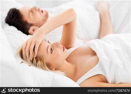 sleeping problems and people concept - unhappy woman lying in bed with snoring man. unhappy woman in bed with snoring sleeping man
