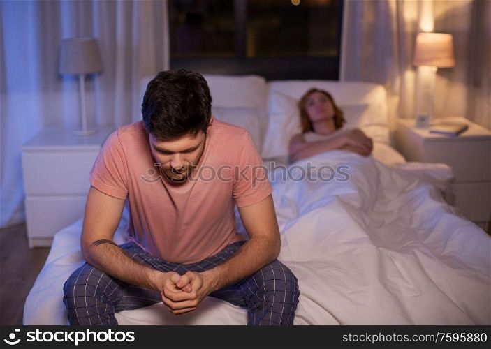 sleeping, rest and people concept - sad man with insomnia sitting on bed at home at night. sad man with insomnia sitting on bed at night