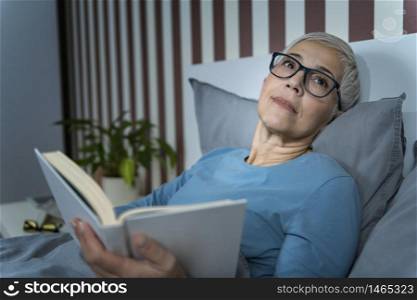Sleeping. Senior woman lying in bed, reading a book before sleep. Sleep. Senior Woman Reading Book in Bed before Sleeping