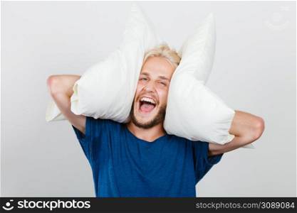 Sleeping well concept. Happy young man rested after good night sleep playing with downy cushion, laughing and having fun. Man playing with pillows, good sleep concept