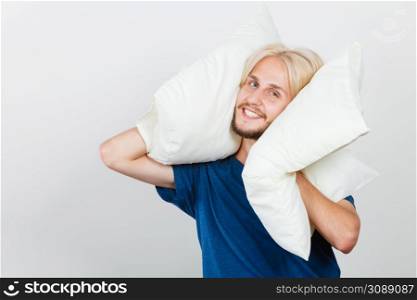 Sleeping well concept. Happy young man rested after good night sleep playing with pillows, smiling having fun. Man playing with pillows, good sleep concept