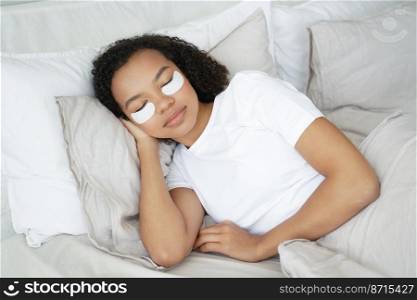 Sleeping young mixed race girl with under eye patches on face relaxing, lying in bed. Pretty woman rests, napping in bedroom, using moisturizing beauty masks. Skincare routine, healthy sleep.. Sleeping young mixed race girl with under eye patches on face relax, lying in bed. Skincare routine