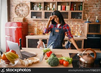 Sleepy black woman in apron cooking healthy breakfast on the kitchen. African female person preparing vegetable salad at home