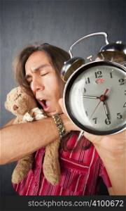 Sleepy handsome young man with long hair and alarm clock