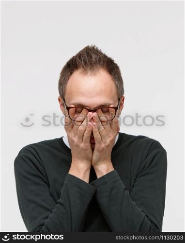 Sleepy man in eyeglasses rubbing her eyes, feels tired after working on laptop, isolated on white background. Overwork, spectacles blurry, chronic fatigue, mental stress, lack of sleep concept