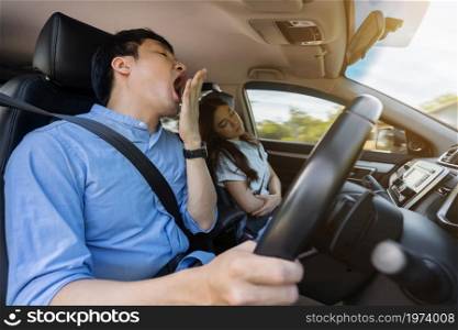 sleepy man yawning while driving a car and his wife is sleeping