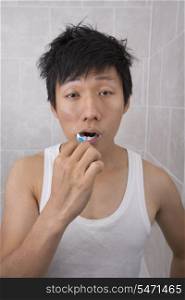 Sleepy mid adult man brushing teeth in bathroom