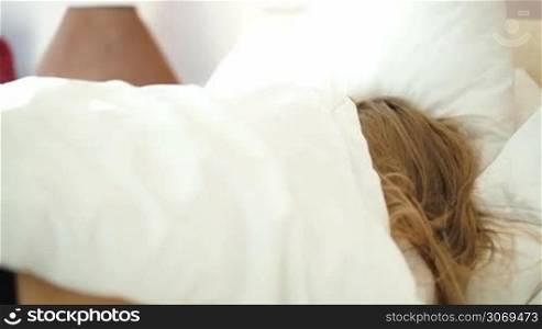 Sleepy woman rolling over the bed and then appearing from under the blanket hardly waking up