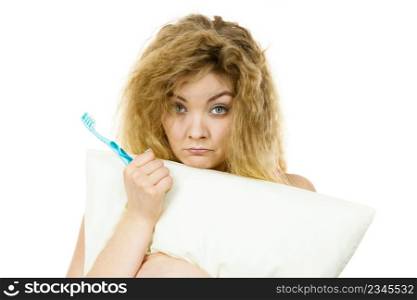 Sleepy woman with blonde tangled hair hugging white pillow holding toothbrush feeling tired or hangover. Studio shot isolated. Sleepy woman hugging white pillow