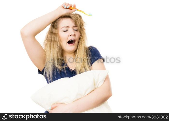 Sleepy woman with blonde tangled hair hugging white pillow holding toothbrush feeling tired or hangover. Studio shot isolated. Sleepy woman hugging white pillow