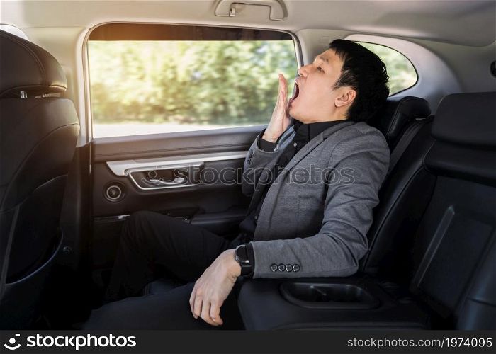 sleepy young business man yawning while sitting in the back seat of car