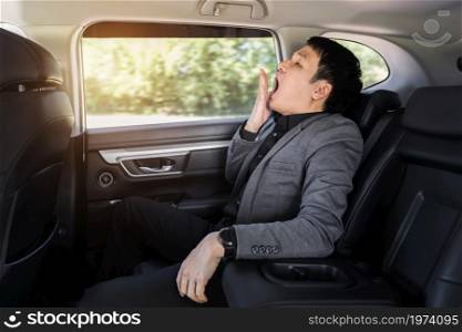 sleepy young business man yawning while sitting in the back seat of car