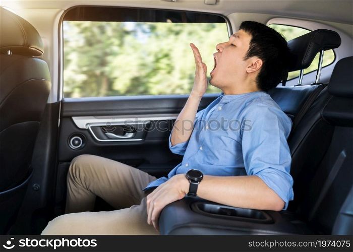 sleepy young man yawning while sitting in the back seat of car