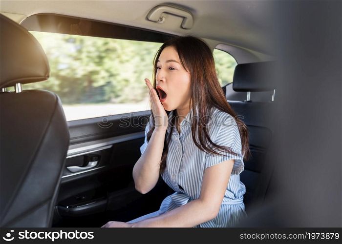 sleepy young woman yawning while sitting in the back seat of car