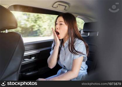 sleepy young woman yawning while sitting in the back seat of car