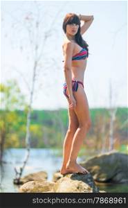 slender brunette posing on a large rock near the lake