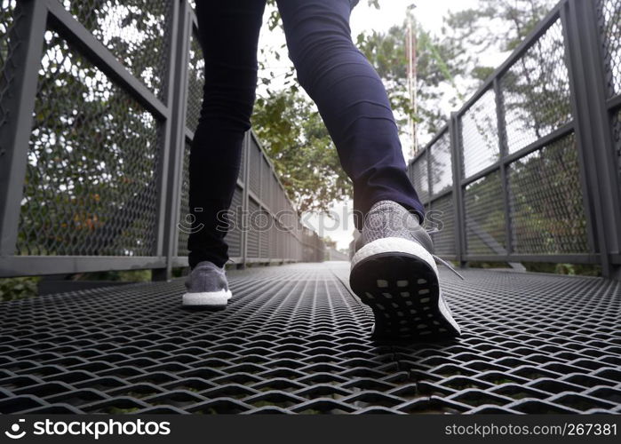 Slender female legs in blue jeans and grey sneakers walking along forest trail