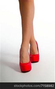 slender female legs in bright red high-heeled shoes and on a light background. legs red heel