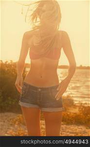 Slender girl in swimsuit and denim shorts warm sunset light
