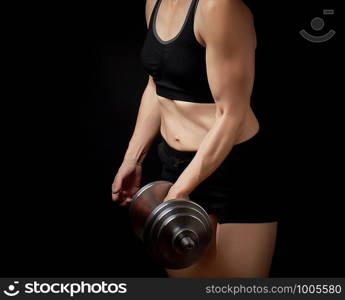 slender girl with a sports figure and muscles holds a type-setting steel dumbbell, she is dressed in a black bra and short shorts, sports backdrop