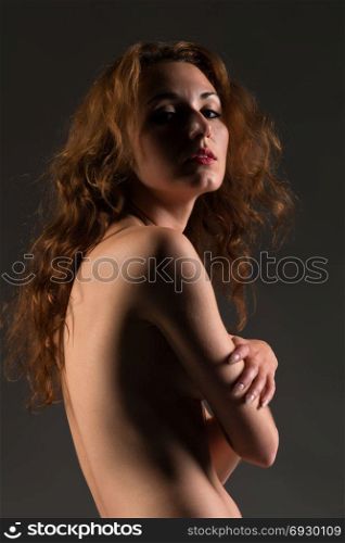 Slender young redheaded woman standing nude on gray