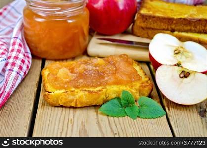 Slice of bread with apple jam and mint, slices of apple, a jar of jam, a napkin on the background of wooden boards