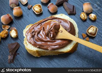Slice of bread with spread chocolate cream and hazelnuts on black table. Serving a delicious breakfast concept.. Hazelnut Nougat cream on slice of bread