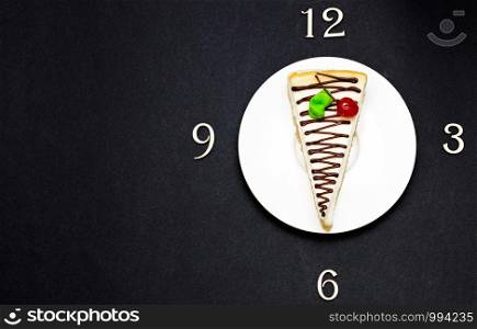 slice of cheesecake and time alphabet letters clock 3 6 9 12 break ceramic white plate top view height plan on dark background.. slice of cheesecake and time alphabet letters clock 3 6 9 12 break ceramic white plate top view height plan on dark background