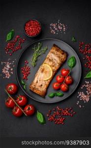 Slice of delicious baked fish with salt, spices and herbs on a ceramic plate on a dark concrete background