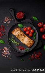 Slice of delicious baked fish with salt, spices and herbs on a ceramic plate on a dark concrete background