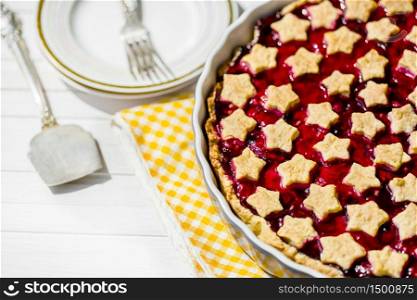 slice of delicious homemade sour cherry pie on plate. Bowl with whipped cream, dessert forks and whole tart on wooden table, classic recipe, view from above. slice of delicious homemade sour cherry pie on plate.