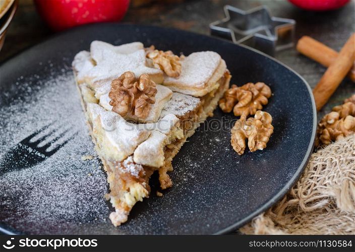 Slice of fresh baked homemade apple pie and walnuts on the black plate