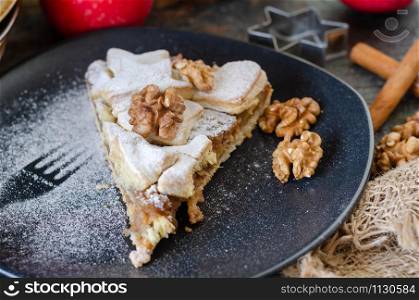 Slice of fresh baked homemade apple pie and walnuts on the black plate
