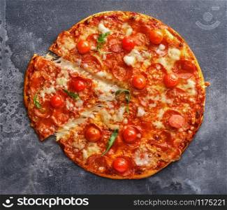 Slice of pepperoni pizza with cherry tomatoes. Sliced tasty pepperoni pizza on the grey stone background. Top view.