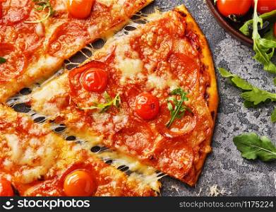 Slice of pepperoni pizza with cherry tomatoes. Sliced tasty pepperoni pizza on the grey stone background. Top view.