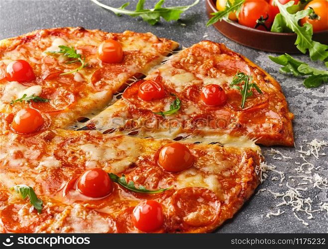 Slice of pepperoni pizza with cherry tomatoes. Sliced tasty pepperoni pizza on the grey stone background.