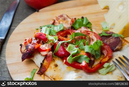 slice of pizza with peppers, bacon and herbs on a round wooden board